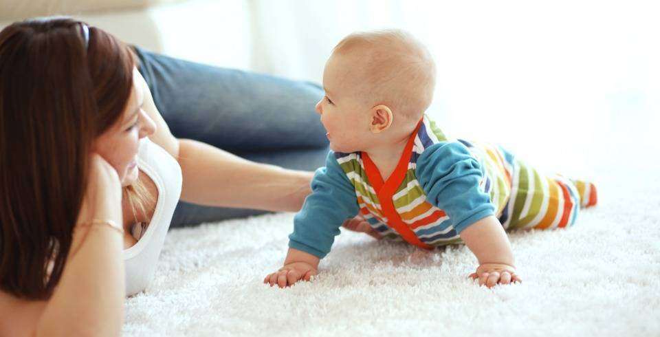 Mama vorbeste cu bebelusul, pe covor